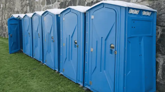 Row of blue portable toilets lined up on grass against a stone wall for event sanitation in Tallahassee, FL