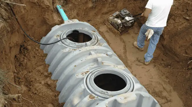 Septic tank installation showing a technician compacting soil around a new poly septic tank in an excavation pit in Tallahassee, FL